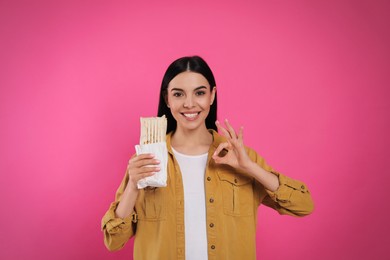 Happy young woman with delicious shawarma on pink background