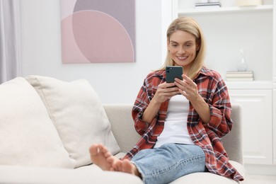 Photo of Happy woman sending message via smartphone on couch at home