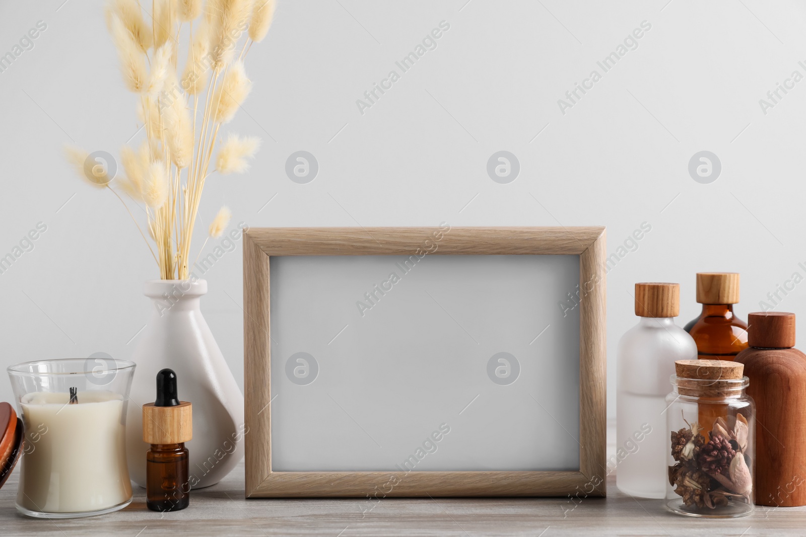 Photo of Blank photo frame, different bottles and decor elements on wooden table