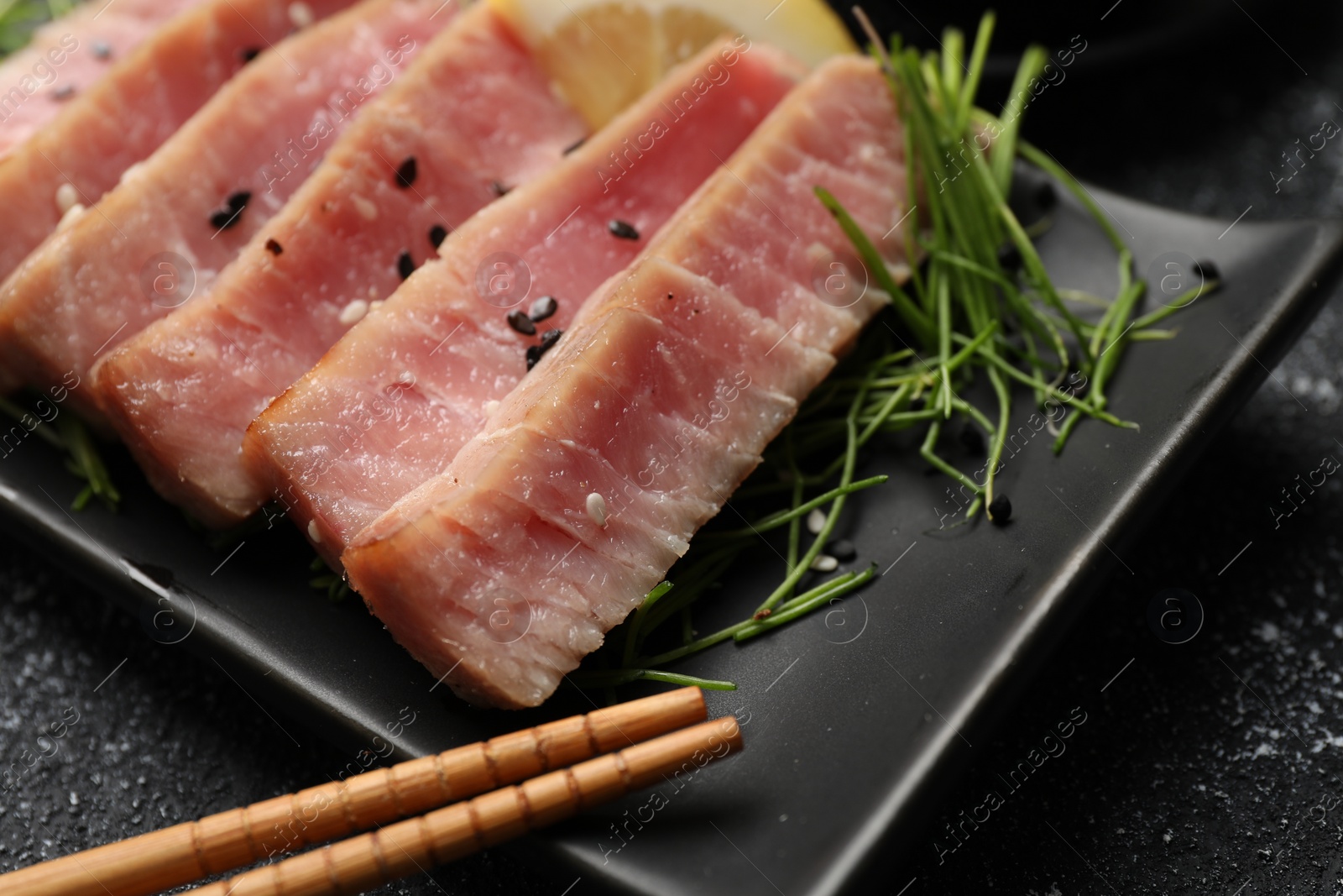 Photo of Pieces of delicious tuna steak served on black table, closeup