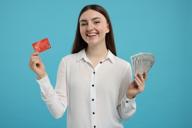 Happy woman with credit card and dollar banknotes on light blue background