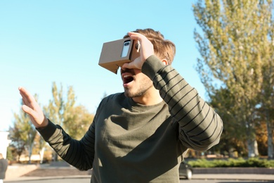 Photo of Young man using cardboard virtual reality headset outdoors