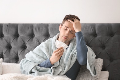 Sick young man with tissue suffering from cold in bed