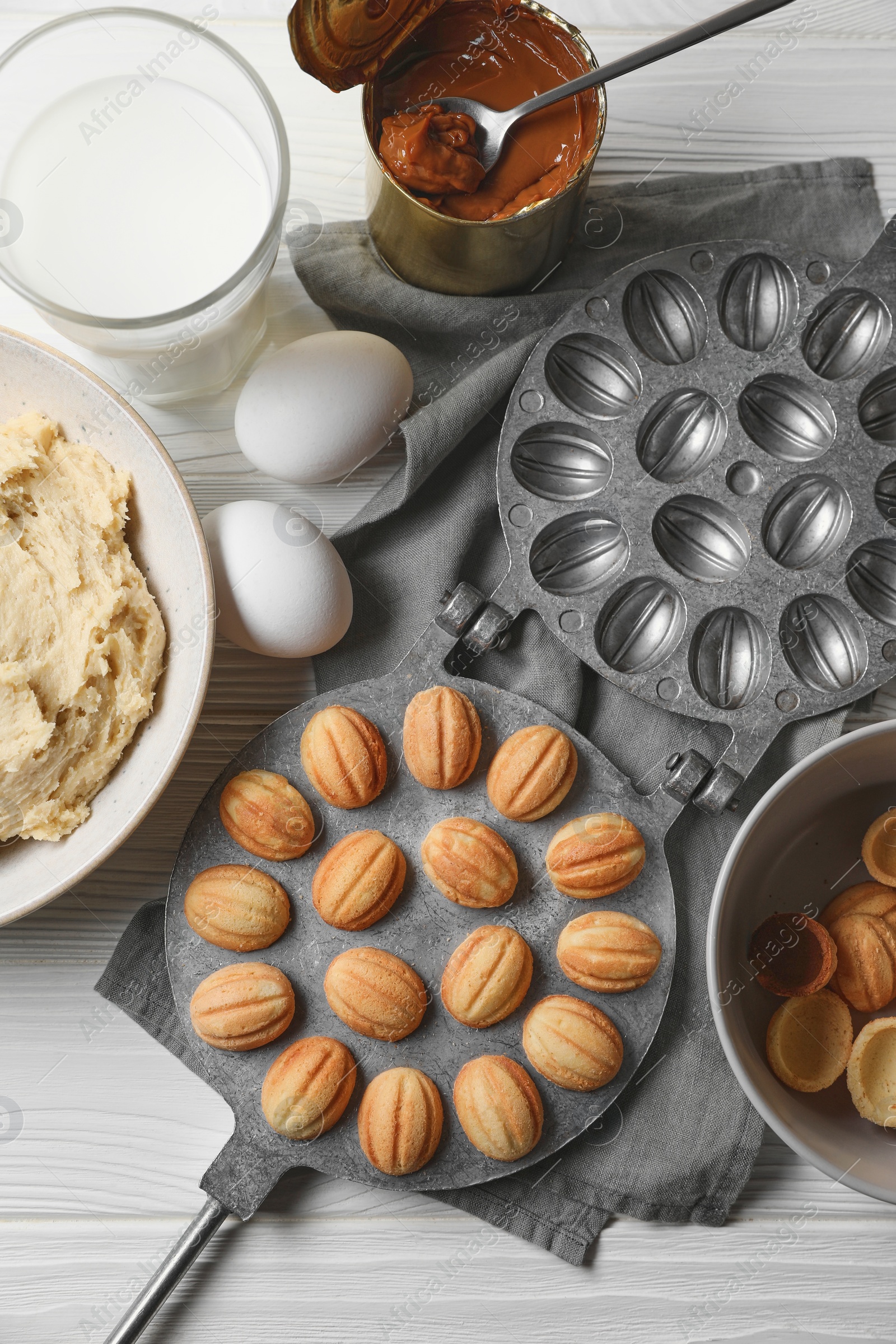 Photo of Delicious walnut shaped cookies with condensed milk and ingredients on white wooden table, flat lay