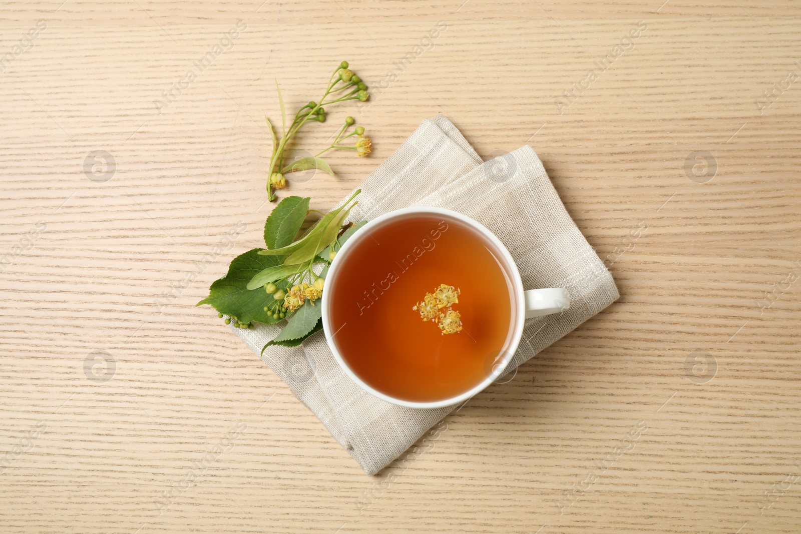 Photo of Cup of tea with linden blossom on wooden table, flat lay
