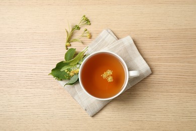 Cup of tea with linden blossom on wooden table, flat lay