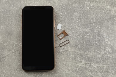 Photo of SIM card, mobile phone, tray and ejector tool on grey table, flat lay. Space for text