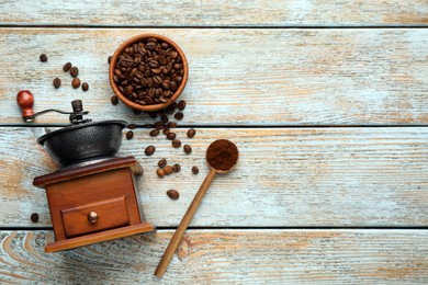 Photo of Vintage manual coffee grinder, powder and beans on wooden table, flat lay. Space for text