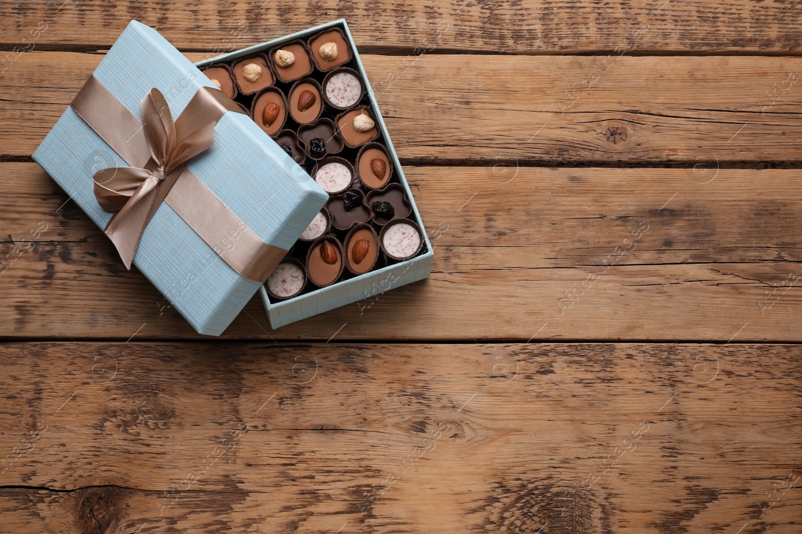 Photo of Open box of delicious chocolate candies on wooden table, top view. Space for text