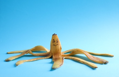 Banana peel with drawn happy face on light blue background
