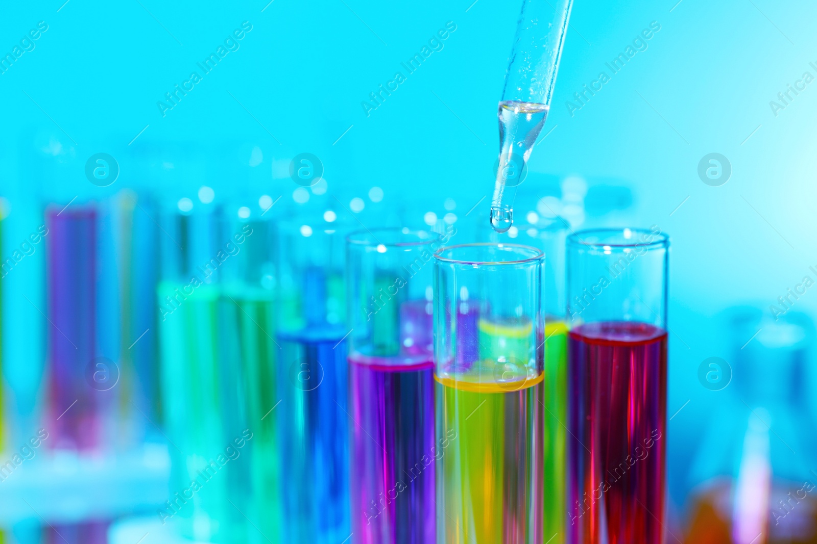 Photo of Dripping liquid from pipette into test tube on light blue background, closeup