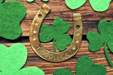 Photo of Decorative clover leaves and horseshoe on wooden background, flat lay. St. Patrick's Day celebration