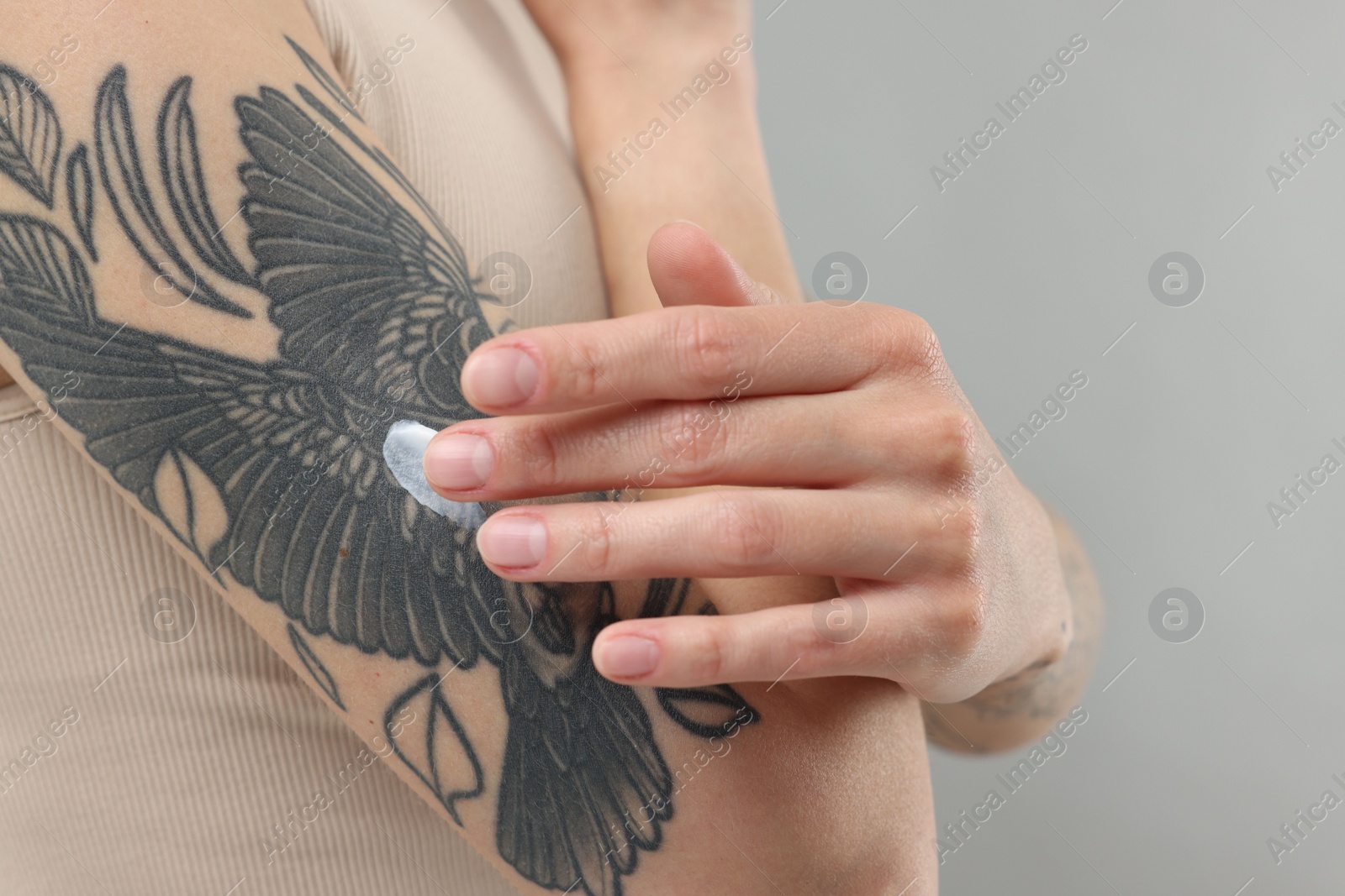 Photo of Tattooed woman applying cream onto her arm on gray background, closeup