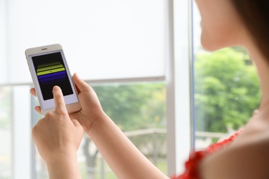 Photo of Woman using smart home application on phone to control window blinds indoors, closeup