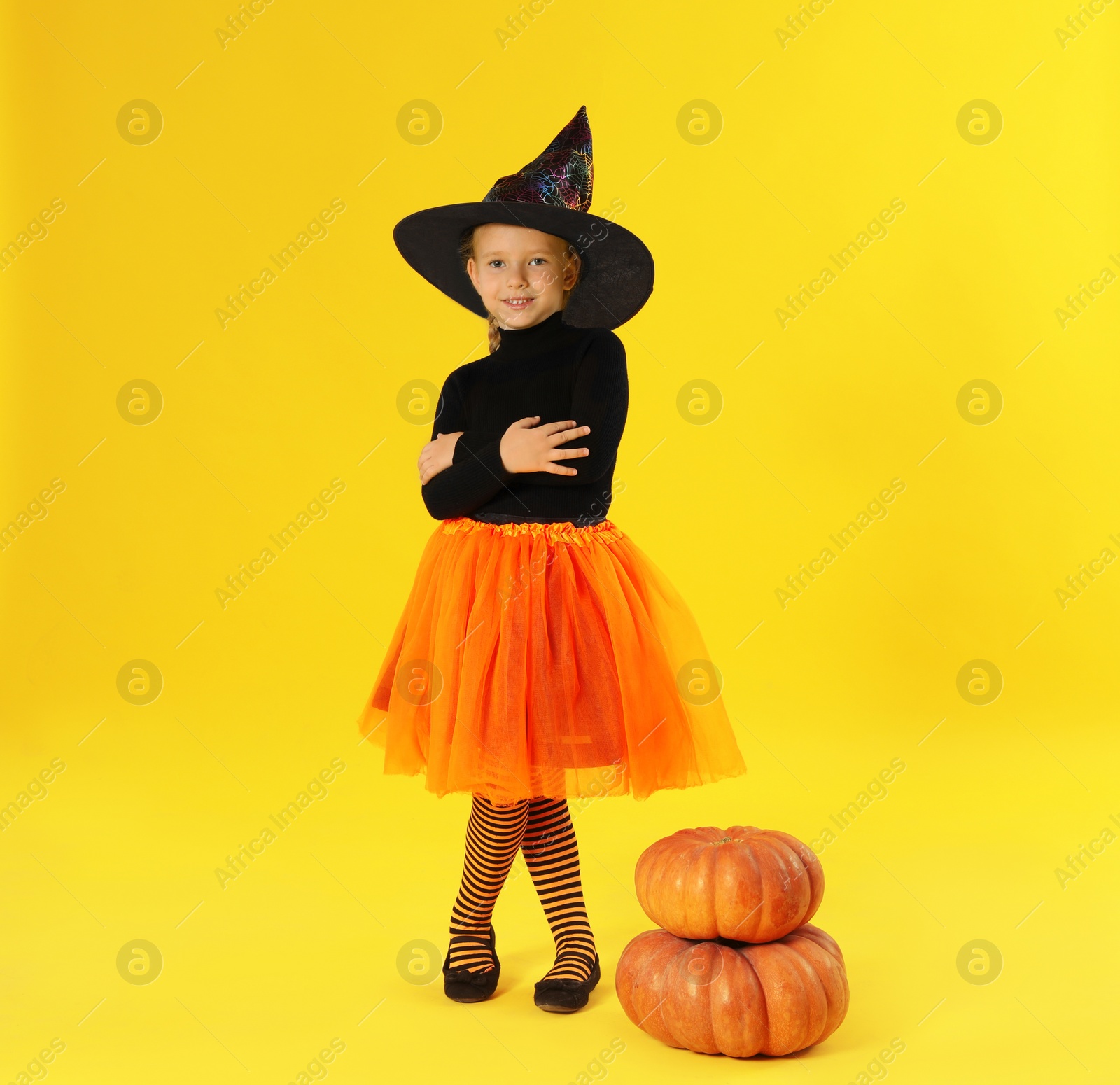 Photo of Cute little girl with pumpkins wearing Halloween costume on yellow background. Space for text