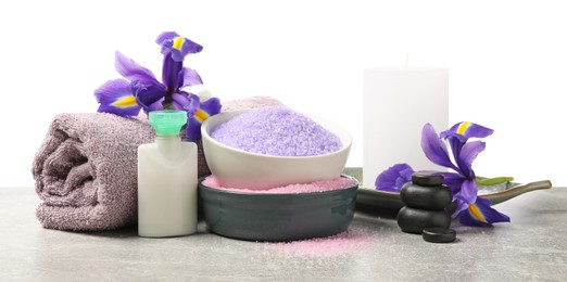 Photo of Different types of sea salt, rolled towel, spa stones, candle and flowers on grey table against white background