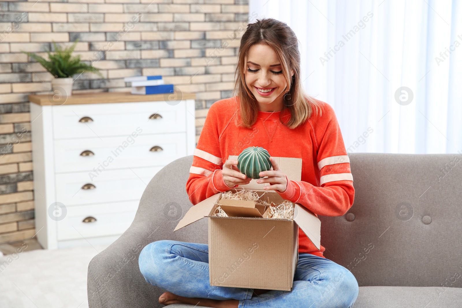 Photo of Young woman opening parcel on sofa in living room