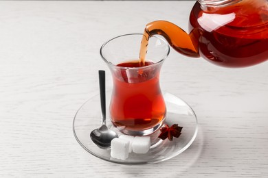 Pouring traditional Turkish tea from pot into glass on white wooden table