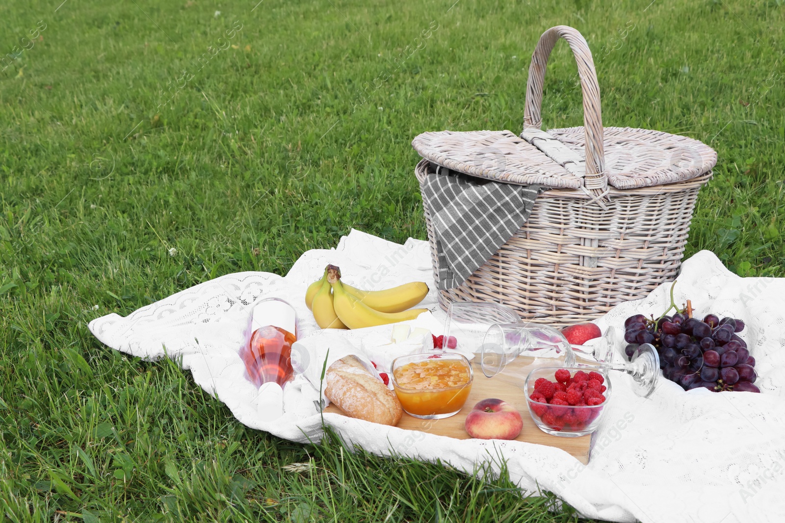 Photo of Picnic blanket with tasty food, basket and cider on green grass outdoors