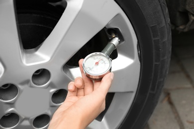 Woman checking car tire pressure with air gauge, closeup