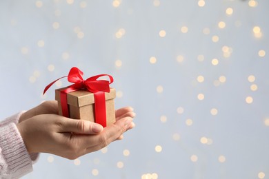 Photo of Woman holding gift box with red bow against blurred festive lights, closeup and space for text. Bokeh effect