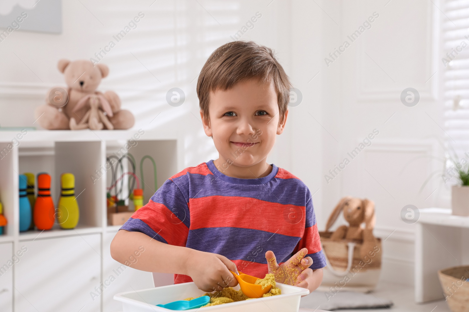 Photo of Cute little boy playing with bright kinetic sand at table in room