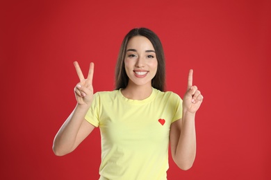 Photo of Woman in yellow t-shirt showing number three with her hands on red background