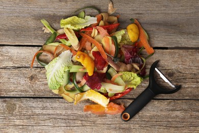 Peels of fresh vegetables and peeler on wooden table, top view