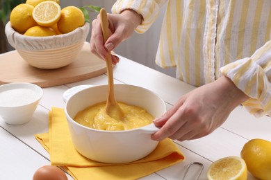 Photo of Woman cooking lemon curd at white wooden table, closeup