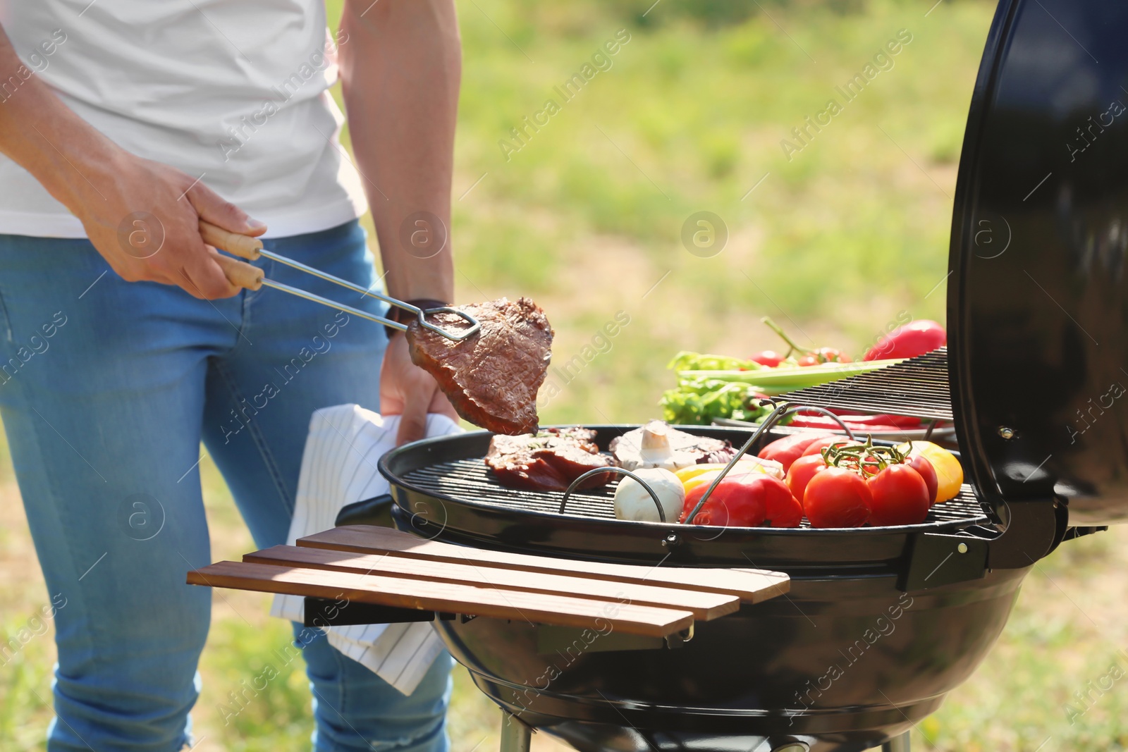 Photo of Man cooking meat and vegetables on barbecue grill outdoors