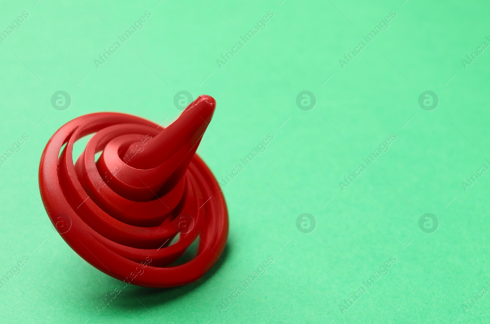 Photo of One red spinning top on green background, closeup. Space for text