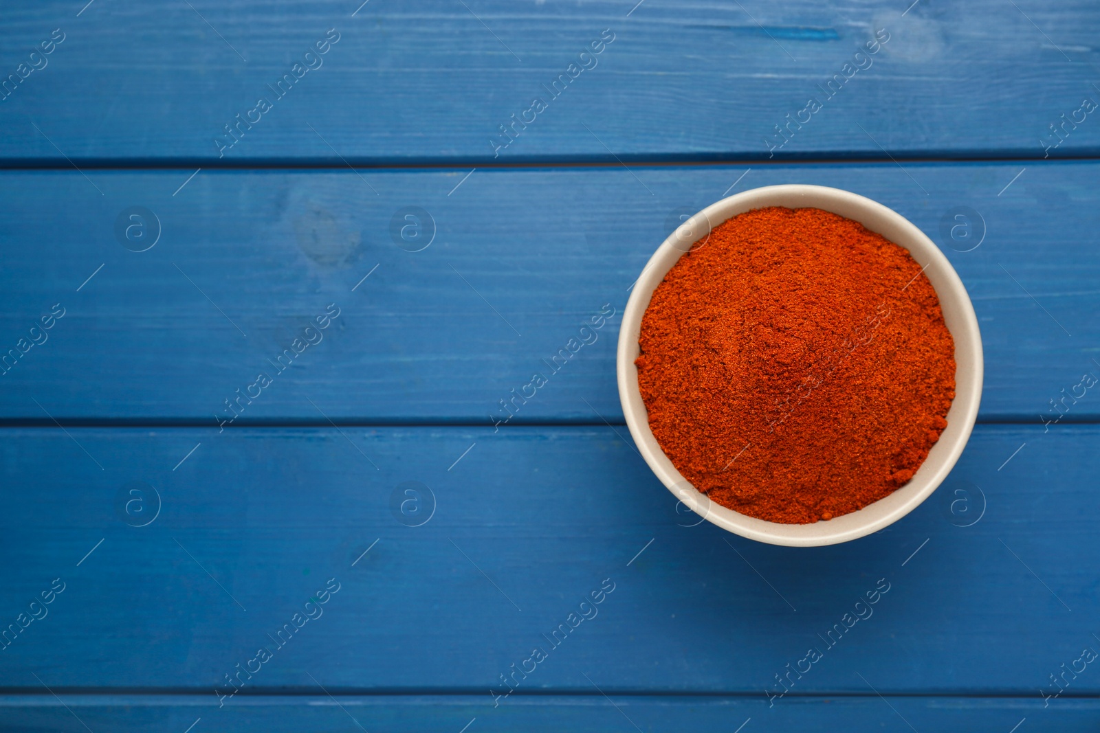 Photo of Bowl with aromatic paprika powder on blue wooden table, top view. Space for text