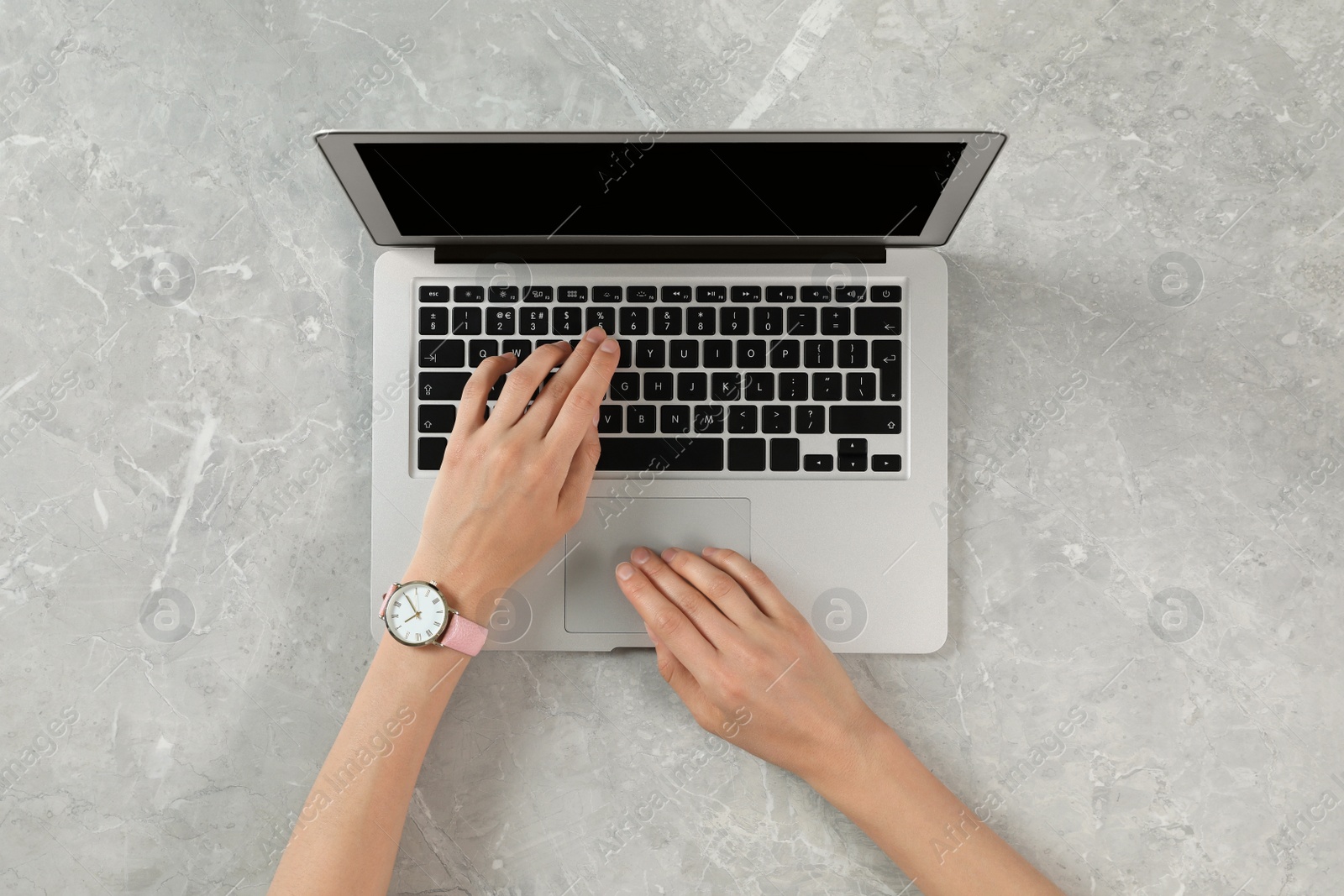 Photo of Woman using modern laptop at marble table, top view