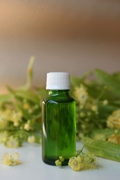 Bottle of essential oil and linden blossoms on white table