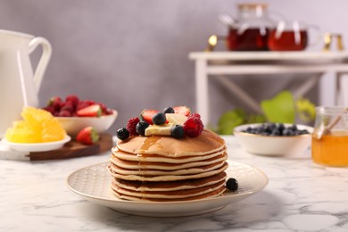 Delicious pancakes with fresh berries, butter and honey on white marble table, space for text