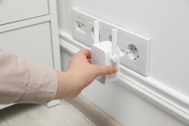 Photo of Woman inserting wireless Wi-Fi repeater into power socket indoors, closeup