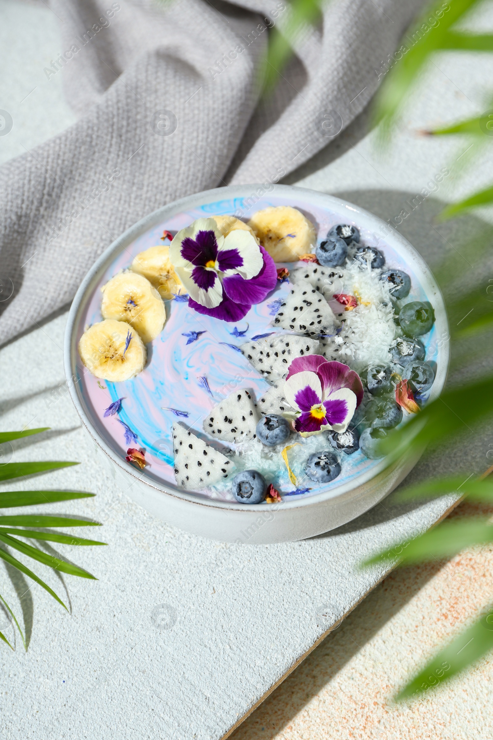 Photo of Delicious smoothie bowl with fresh fruits, blueberries and flowers on color textured table