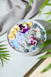 Delicious smoothie bowl with fresh fruits, blueberries and flowers on color textured table