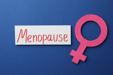 Card with word Menopause and female gender sign on blue background, flat lay