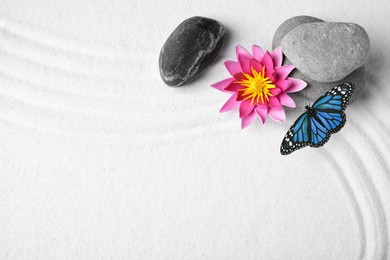 Beautiful butterfly, flowers and stones on white sand with pattern, flat lay. Zen concept