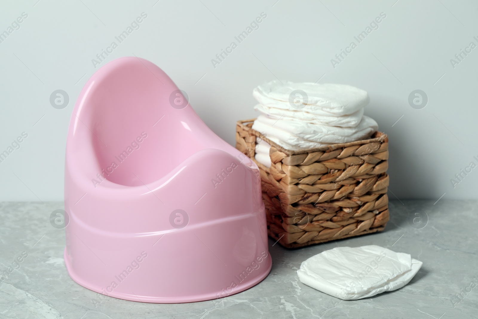 Photo of Pink baby potty and diapers near light wall. Toilet training