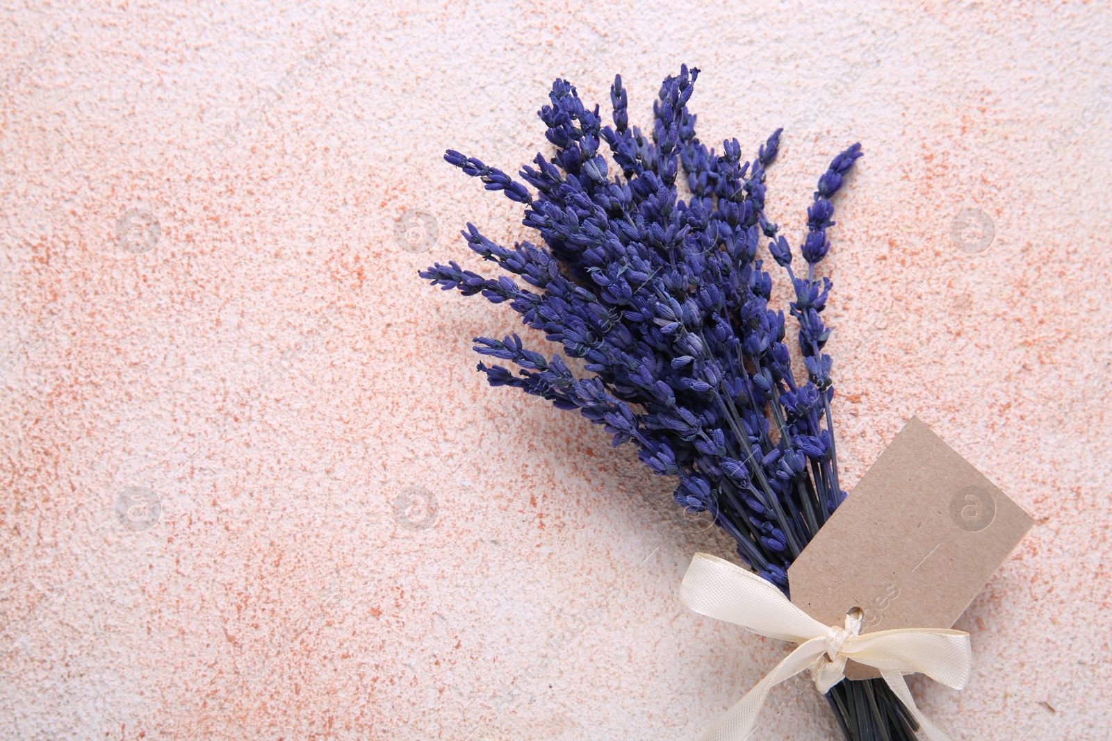 Photo of Bouquet of beautiful preserved lavender flowers with blank tag and ribbon on color textured table, top view. Space for text