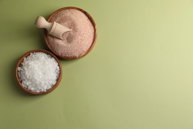 Different natural salt on green background, flat lay. Space for text