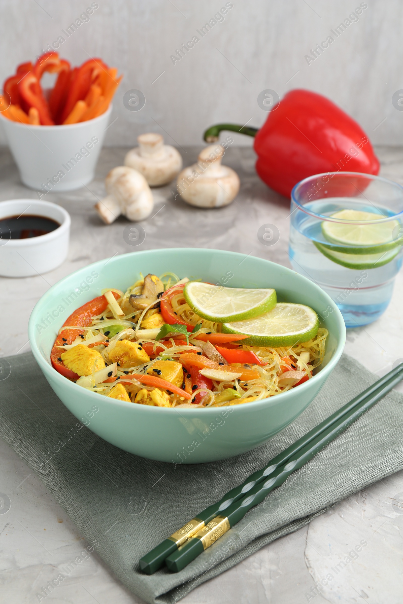 Photo of Stir-fry. Delicious cooked noodles with chicken and vegetables in bowl served on gray textured table