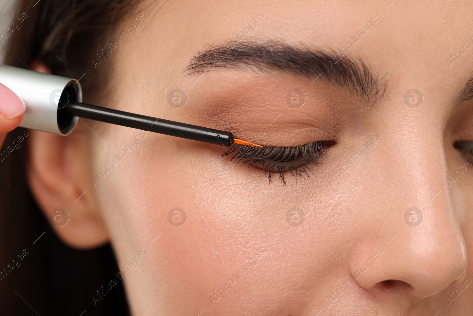 Photo of Woman applying serum onto her eyelashes, closeup. Cosmetic product