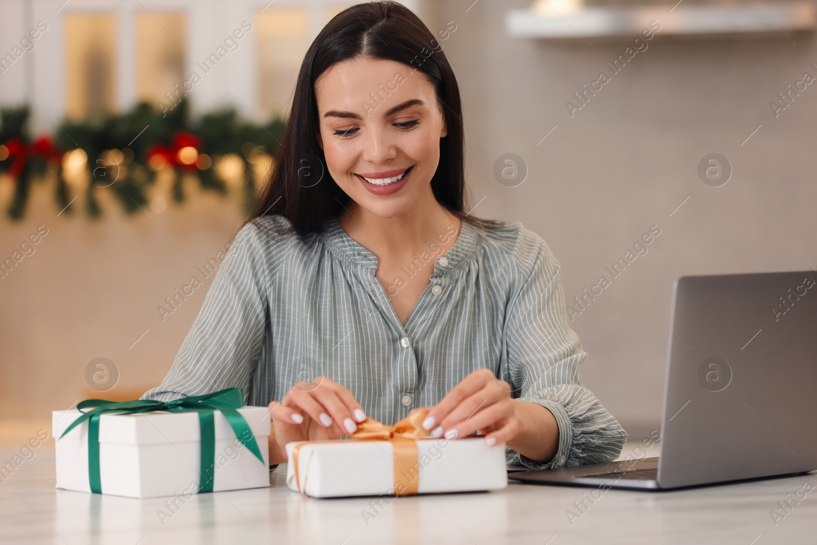 Photo of Celebrating Christmas online with exchanged by mail presents. Smiling woman opening gift box during video call on laptop at home