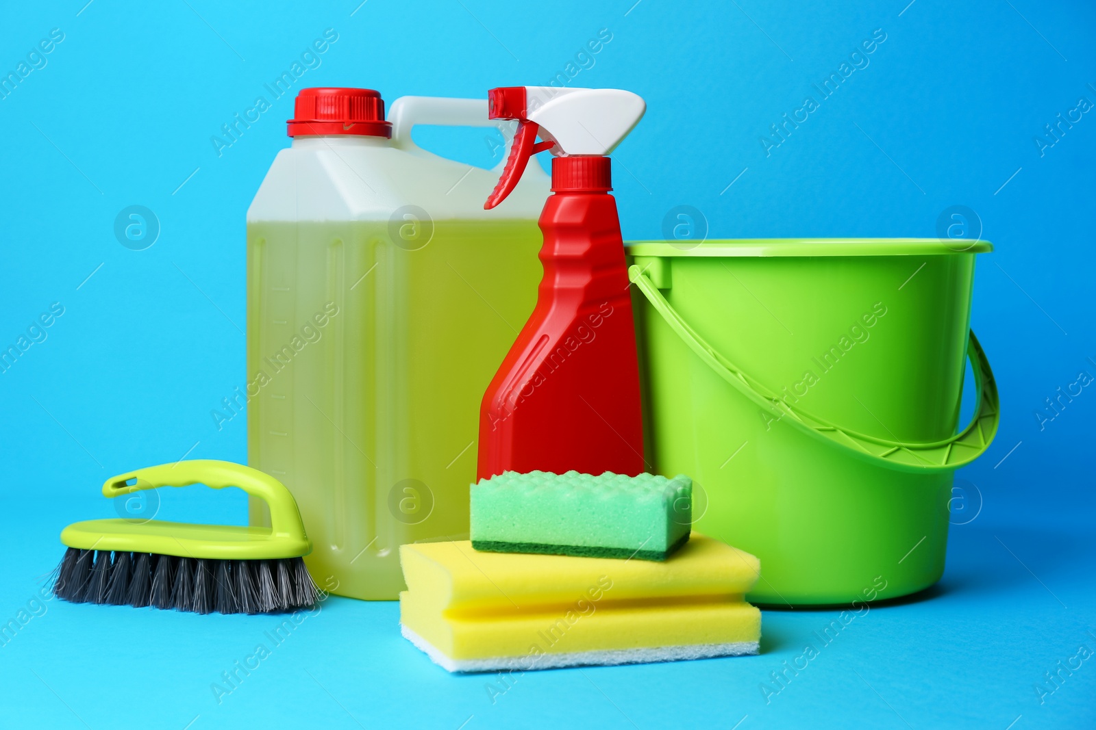 Photo of Green bucket, cleaning supplies and tools on light blue background