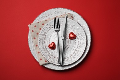 Photo of Beautiful place setting with dishware and sweets for romantic dinner on red table, top view