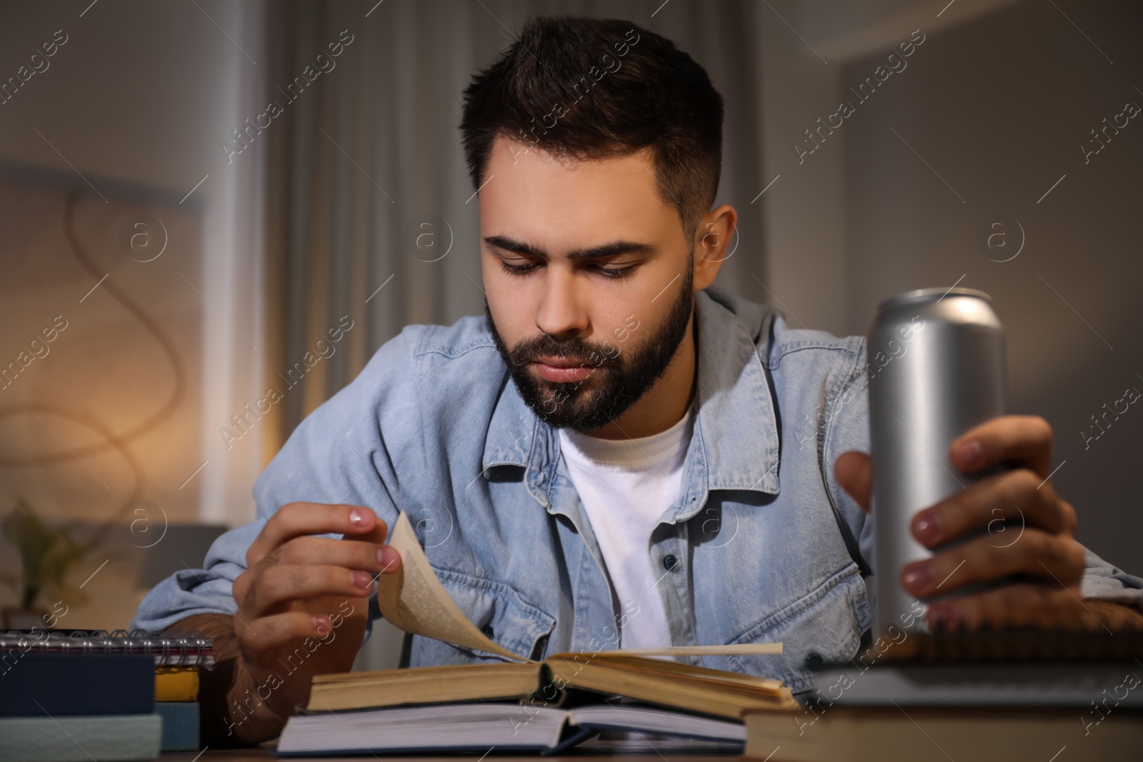 Photo of Tired young man with energy drink studying at home