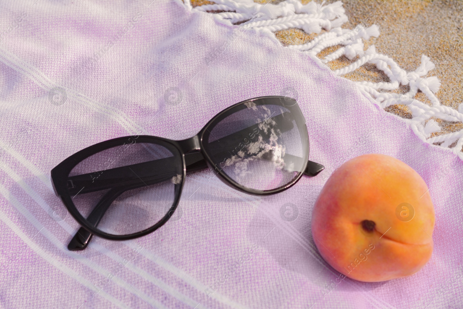 Photo of Beautiful sunglasses and peach on blanket, closeup